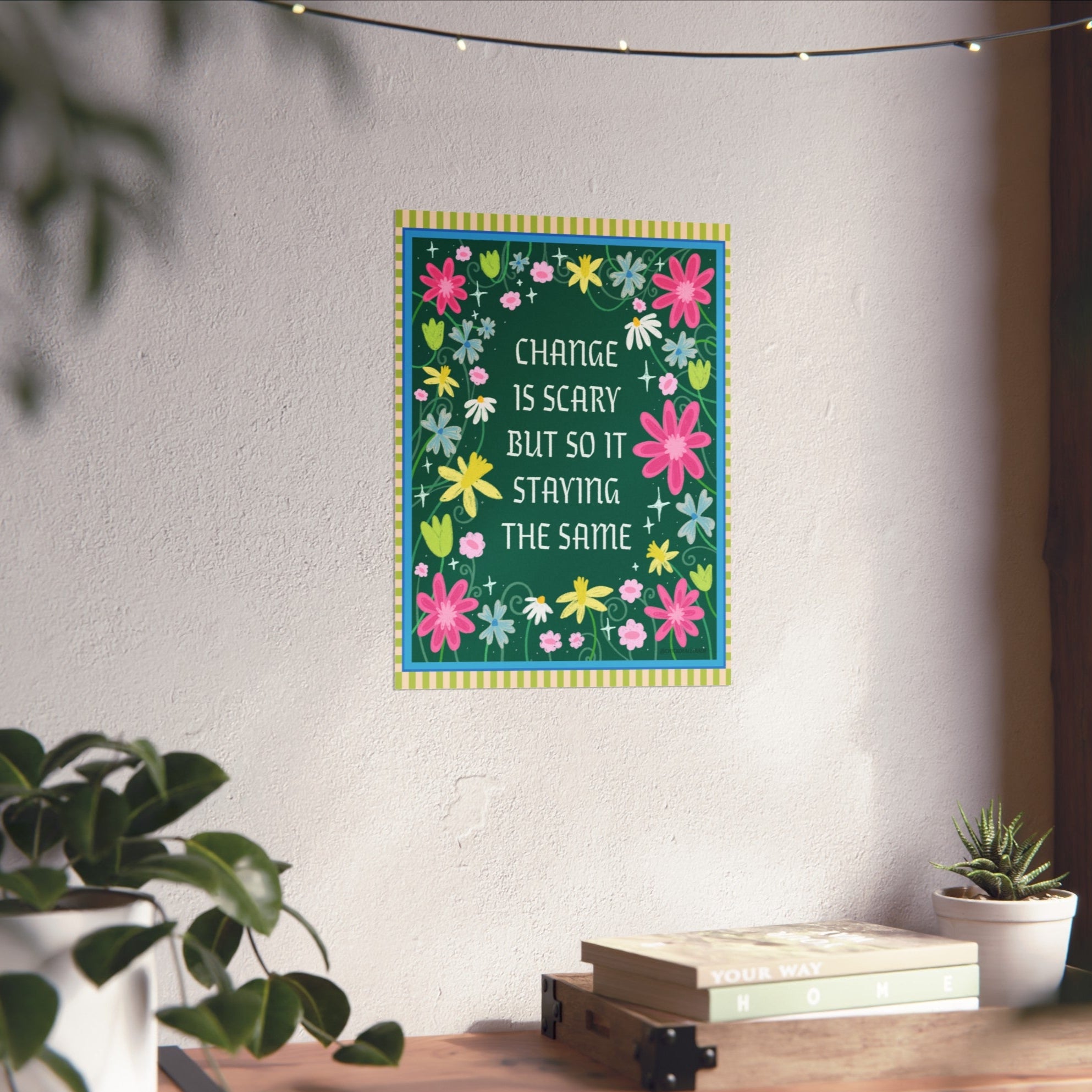 Decorative wall art with floral design and motivational quote on a white wall with plants and books below.