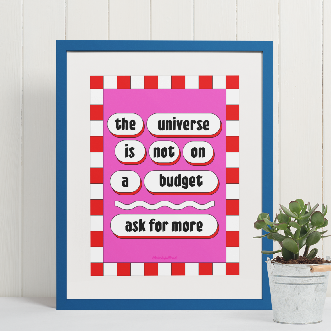 Framed poster with motivational quote on a white wall with a plant below